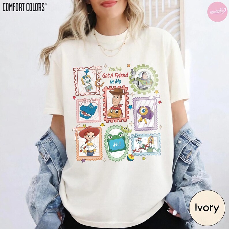May include: An ivory short-sleeve t-shirt featuring a graphic print of various Toy Story characters framed in postage stamp-style borders. The text "You've Got A Friend In Me" is centered among illustrations of Woody, Buzz Lightyear, Jessie, and other characters.