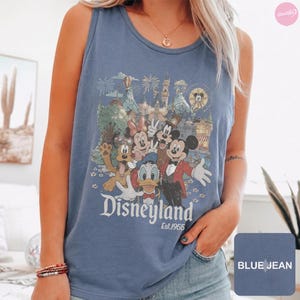 May include: A blue denim-colored tank top featuring a graphic print of Mickey Mouse, Minnie Mouse, Donald Duck, and Pluto in front of a castle. The text "Disneyland" and "Est. 1955" is printed below the characters in a white, stylized font.