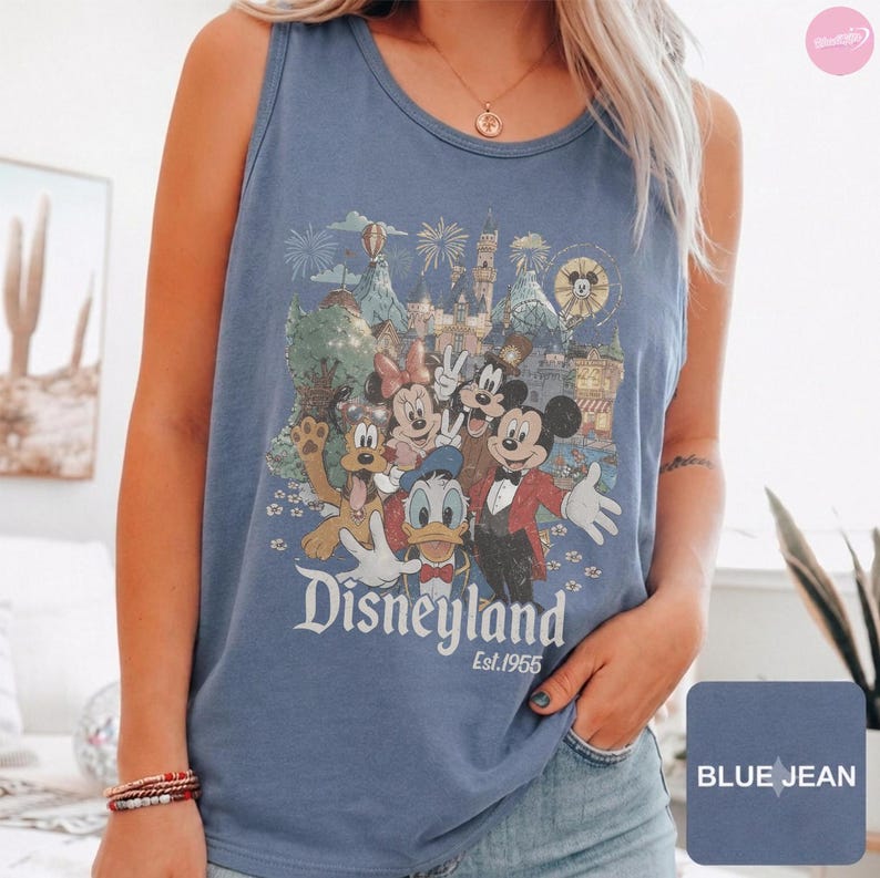 May include: A blue denim-colored tank top featuring a graphic print of Mickey Mouse, Minnie Mouse, Donald Duck, and Pluto in front of a castle. The text "Disneyland" and "Est. 1955" is printed below the characters in a white, stylized font.