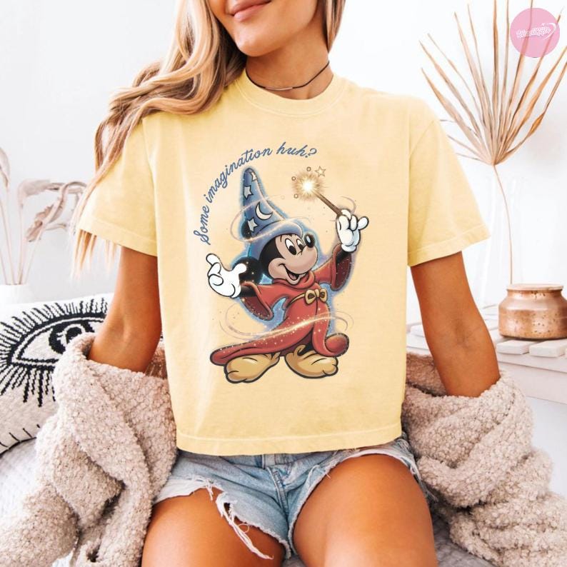 K&ouml;nnte beinhalten: Hellgelbes T-Shirt mit einer Cartoon-Abbildung von Mickey Mouse als Zauberer, der einen Zauberstab h&auml;lt. Der Text "Some imagination huh?" steht &uuml;ber der Figur. Das T-Shirt hat kurze &Auml;rmel und eine lockere Passform.