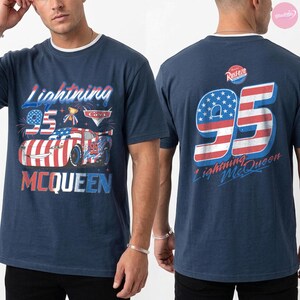 May include: Navy blue t-shirt with a white crew neck featuring a graphic of Lightning McQueen race car with the number 95 and the text "Lightning McQueen". The back of the shirt displays the number 95 in red and white stripes and blue stars.