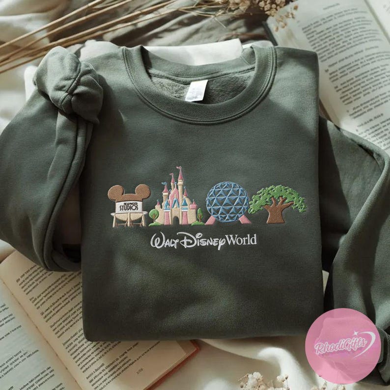 Peut inclure: Sweat-shirt vert olive avec broderie Walt Disney World. Le motif comprend Mickey Mouse, le ch&acirc;teau de Cendrillon, Spaceship Earth et un arbre. Les mots "Walt Disney World" sont brod&eacute;s en dessous.