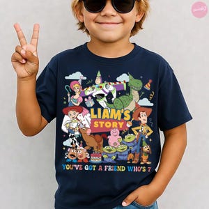 May include: Navy blue t-shirt featuring a colorful graphic of characters from a popular animated movie. The design includes the text "LIAM'S STORY" and "YOU'VE GOT A FRIEND WHO'S 7". The shirt is a children's birthday theme.