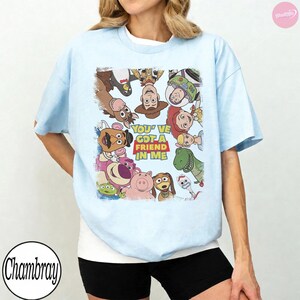 May include: Light blue t-shirt featuring a colorful graphic of characters from the animated film Toy Story. The graphic includes Woody, Buzz Lightyear, Jessie, and others, with the text "You've Got a Friend in Me".