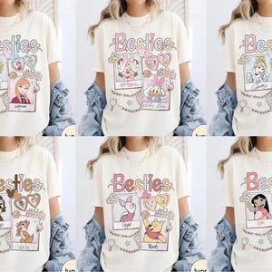 Puede incluir: Camisetas color crema con la palabra "Besties" en fuente cursiva. Cada camiseta presenta un par diferente de personajes de dibujos animados en marcos estilo polaroid, con corazones y estrellas decorativas. Las camisetas son parte de una colecci&oacute;n tem&aacute;tica de Disney.