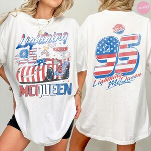 May include: White t-shirt featuring a graphic of Lightning McQueen from the Cars movie. The design includes the number 95, the character's name, and patriotic red, white, and blue colors. The back of the shirt also displays the number 95 and Lightning McQueen.