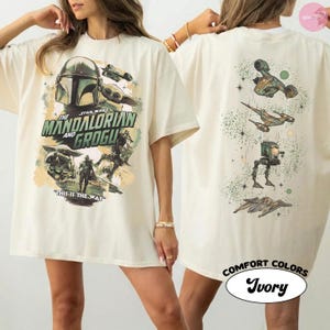 Puede incluir: Camiseta de color marfil con gr&aacute;ficos de la serie "The Mandalorian". La parte delantera muestra el t&iacute;tulo y los personajes, mientras que la parte trasera presenta varias naves espaciales y un dise&ntilde;o de puntos verdes. La camiseta est&aacute; etiquetada como "Comfort Colors".