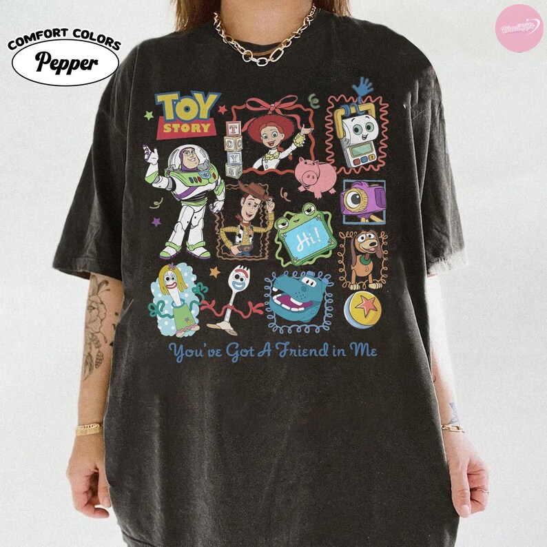 May include: A charcoal gray short-sleeve t-shirt featuring a graphic print of Toy Story characters including Buzz Lightyear, Woody, Jessie, and Forky. The design includes colorful illustrations of various movie icons and the text You've Got A Friend in Me.