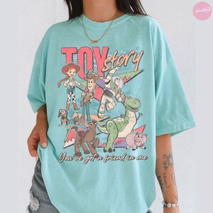 Puede incluir: Camiseta azul claro con el t&iacute;tulo "Toy Story" en rosa y un gr&aacute;fico de personajes de la pel&iacute;cula. La frase "You've got a friend in me" est&aacute; impresa debajo.