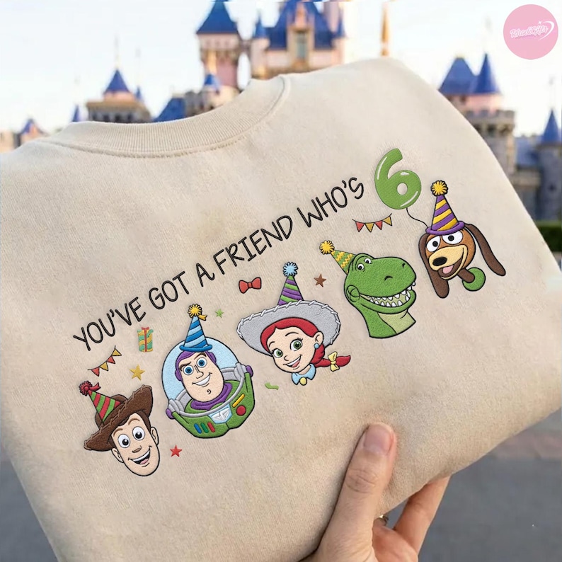 K&ouml;nnte beinhalten: Beiges Sweatshirt mit dem Schriftzug "YOU'VE GOT A FRIEND WHO'S 6" und Cartoonfiguren mit Partyh&uuml;ten. Das Design zeigt Woody, Buzz Lightyear, Jessie, Rex und Slinky Dog, mit einem gr&uuml;nen Ballon.