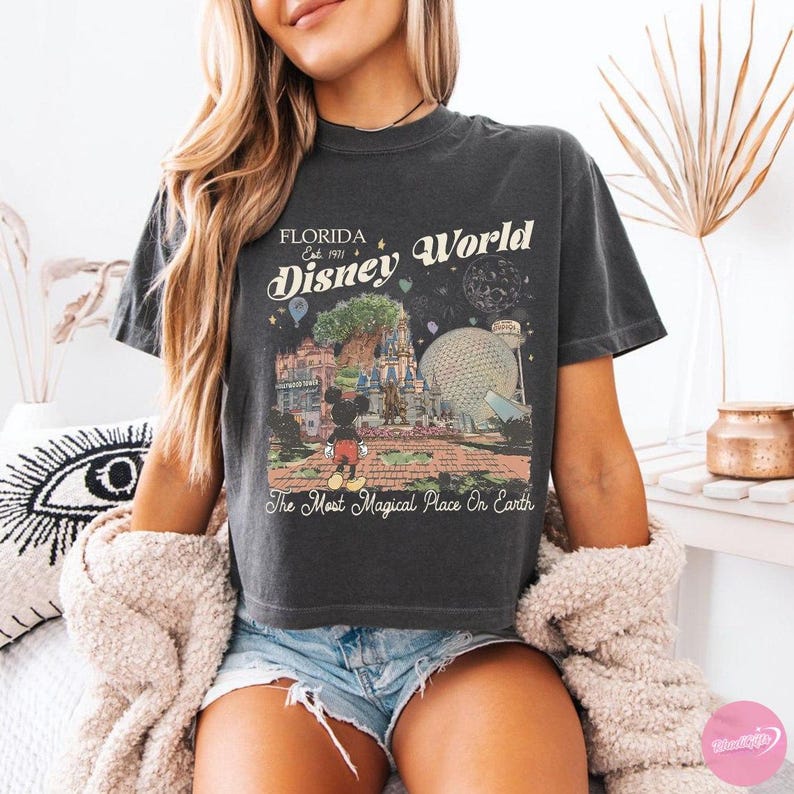 May include: Dark gray t-shirt featuring a vintage-style graphic of Disney World in Florida. The design includes the text "Florida Disney World Est. 1971" and "The Most Magical Place On Earth" with an image of Mickey Mouse.