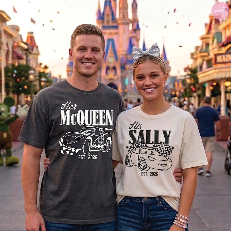 May include: Two people wearing matching t-shirts with car graphics. One shirt says "Her McQueen" and the other says "His Sally", both with "EST. 2026". The shirts are dark gray and cream-colored, respectively. The background shows a castle and a street.