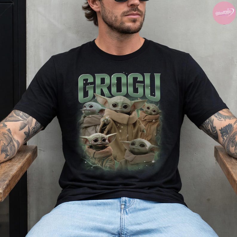 May include: Black t-shirt featuring the word "GROGU" in green block letters above a graphic of Grogu, also known as Baby Yoda, from The Mandalorian. The graphic shows Grogu in various poses. The t-shirt is made of a soft material.