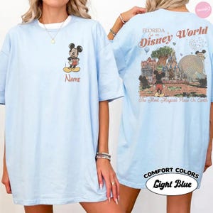 Puede incluir: Camiseta azul claro con Mickey Mouse en la parte delantera y la palabra "Name" debajo. La parte trasera muestra un dise&ntilde;o de Disney World con el texto "Florida Disney World" y "The Most Magical Place On Earth".