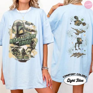 Puede incluir: Camiseta azul claro con dise&ntilde;o de Star Wars: The Mandalorian y Grogu. El frente muestra al Mandaloriano, Grogu y naves espaciales. La parte trasera muestra naves espaciales y el texto "Comfort Colors Light Blue".