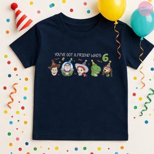 K&ouml;nnte beinhalten: Marineblaues T-Shirt mit Toy Story-Charakteren und dem Text "YOU'VE GOT A FRIEND WHO'S 6". Die Zahl 6 ist gr&uuml;n. Partyh&uuml;te und Luftballons sind im Hintergrund zu sehen. Geeignet f&uuml;r einen Kindergeburtstag.
