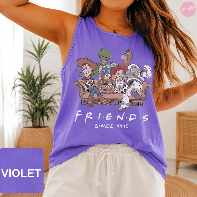 May include: A violet tank top featuring a graphic print of Toy Story characters sitting on a couch with the text "FRIENDS SINCE 1995" printed below. The characters include Woody, Buzz Lightyear, Jessie, Rex, Bullseye, and Mr. Potato Head.
