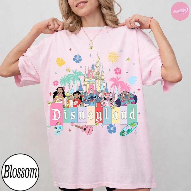 Pu&ograve; includere: T-shirt rosa chiaro con grafica colorata di Disneyland. La grafica include personaggi dei cartoni animati, un castello, palme e la scritta "Disneyland". La maglietta ha maniche corte e una vestibilit&agrave; ampia.