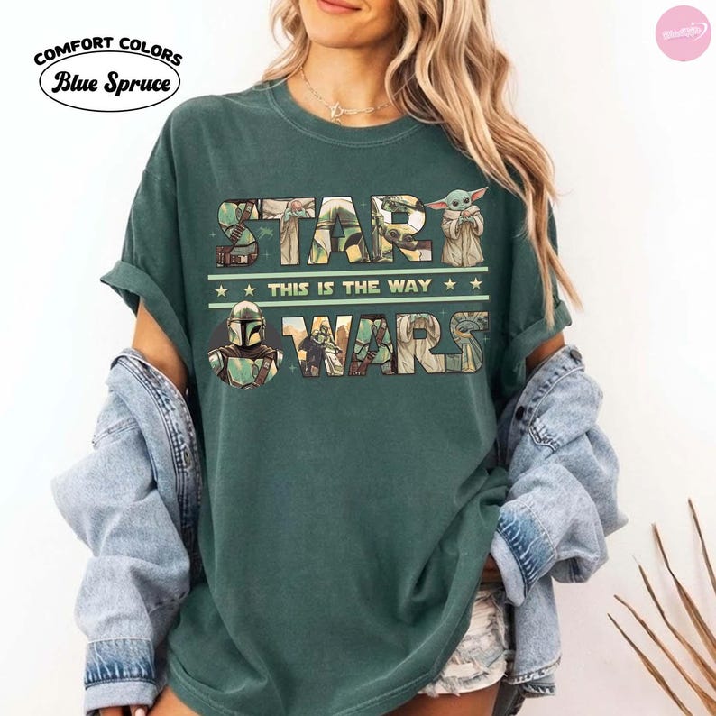 Puede incluir: Camiseta verde oscuro con el texto "STAR WARS" en un dise&ntilde;o de letras en bloque, con im&aacute;genes de personajes y la frase "THIS IS THE WAY". La camiseta tambi&eacute;n tiene los logotipos de Comfort Colors y Blue Spruce.