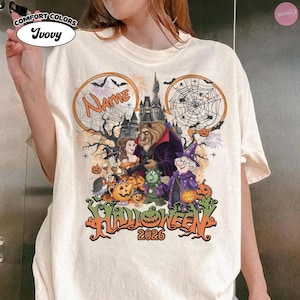 May include: An ivory t-shirt featuring a graphic print of characters from Beauty and the Beast in a Halloween setting. The design includes a castle, spiderwebs, pumpkins, and the text "Name" and "Halloween 2026" in orange and black lettering.