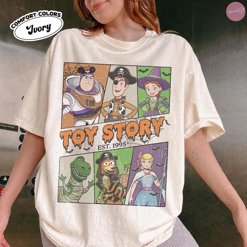 May include: An ivory short-sleeve t-shirt featuring a graphic print of Toy Story characters in Halloween costumes. The design includes Buzz Lightyear, Woody, Jessie, Rex, Slinky Dog, and Bo Peep with the text Toy Story Est. 1995 in a dripping font.
