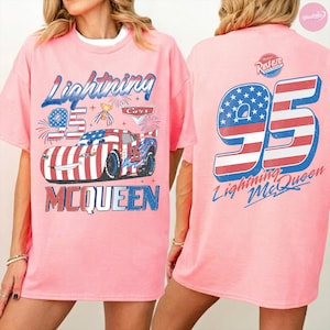May include: Pink t-shirt featuring a graphic of Lightning McQueen from the Cars movie. The front design includes the number 95, the name "Lightning McQueen," and a patriotic car design. The back of the shirt also displays the number 95 and the name "Lightning McQueen."