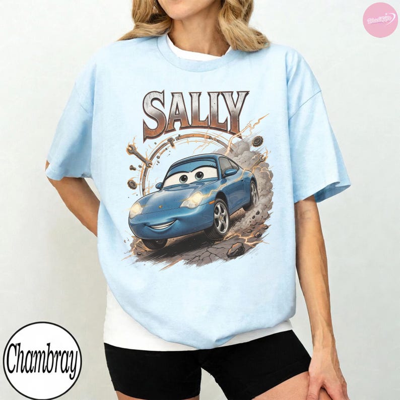 May include: Light blue t-shirt featuring a graphic of Sally Carrera from the movie Cars. The design includes the name "SALLY" in a brown, vintage-style font above the car image. The shirt has a crew neck and short sleeves.