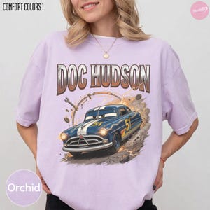 May include: Orchid Comfort Colors t-shirt featuring a graphic of Doc Hudson's car from the movie Cars. The design includes the text "DOC HUDSON" above the car, with a racing number "51" on the car's side.