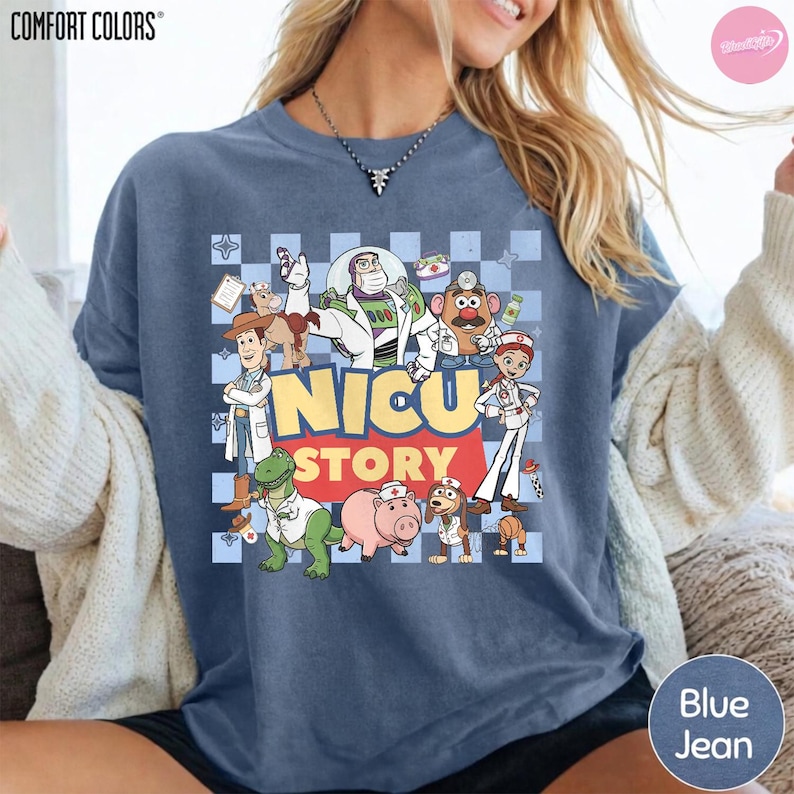 Puede incluir: Una camiseta azul de manga corta con un estampado gr&aacute;fico de varios personajes de dibujos animados vestidos como personal m&eacute;dico. El texto NICU STORY est&aacute; impreso en letras grandes amarillas y rojas sobre un fondo de cuadros azul claro.