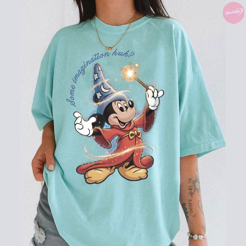K&ouml;nnte beinhalten: Hellblaues T-Shirt mit einer Grafik von Mickey Mouse in einem Zauberer-Outfit, der einen Zauberstab mit einem Funkel-Effekt h&auml;lt. Der Text "Some imagination huh?" ist &uuml;ber der Grafik aufgedruckt. Das T-Shirt hat kurze &Auml;rmel.