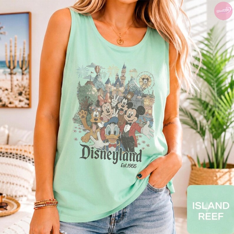 May include: A light mint green sleeveless tank top featuring a graphic print of Disney characters including Mickey Mouse, Minnie Mouse, Donald Duck, and Pluto in front of a castle. The text Disneyland Est. 1955 is printed below the characters.