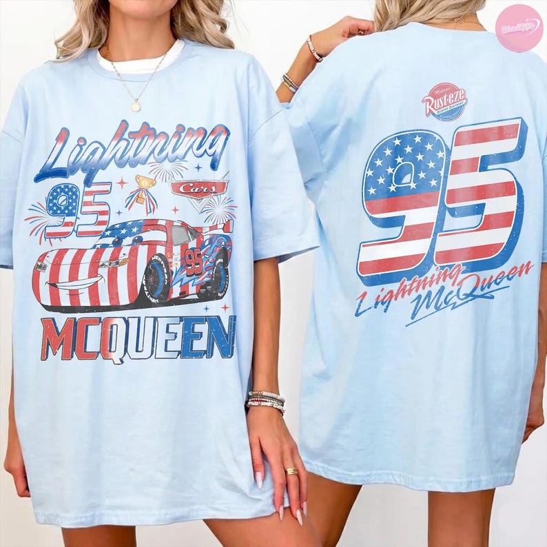 May include: Light blue t-shirt featuring a graphic of Lightning McQueen from the Cars movie. The front design includes the text "Lightning 95 McQueen" with a race car illustration. The back of the shirt displays a large "95" with an American flag design and "Lightning McQueen" text.