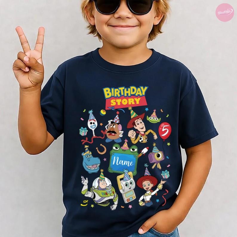 May include: A navy blue short-sleeve t-shirt featuring a colourful graphic with the text "BIRTHDAY STORY" and "Name" inside a green frame. The design includes various cartoon characters wearing party hats, a red balloon with the number 5, and confetti.
