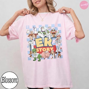 Puede incluir: Una camiseta rosa claro con un estampado gr&aacute;fico de personajes de Toy Story vestidos como personal m&eacute;dico. El dise&ntilde;o incluye a Buzz Lightyear, Woody, Rex, Hamm y el Sr. Patata con el texto ER STORY en letras amarillas grandes sobre una cuadr&iacute;cula azul.