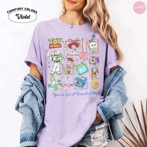 May include: A violet short-sleeve t-shirt featuring a graphic print of Toy Story characters including Buzz Lightyear, Woody, Jessie, and others. The text Toy Story and You've Got A Friend in Me are printed on the front. The shirt is made by Comfort Colors.