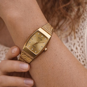 Vintage gold tone women’s watch from the 1980s worn on a female wrist, featuring a rectangular case and elegant gold bracelet