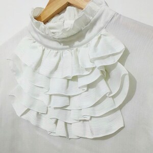 May include: White blouse with a large, layered ruffle collar.
