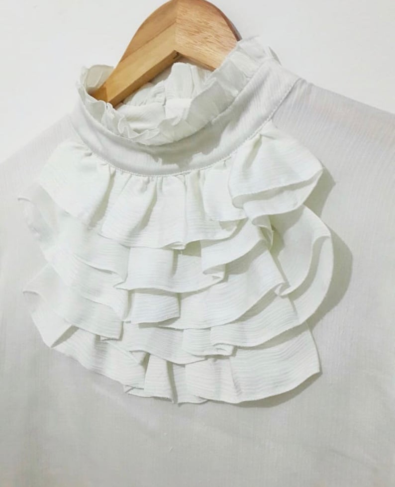 May include: White blouse with a large, layered ruffle collar.