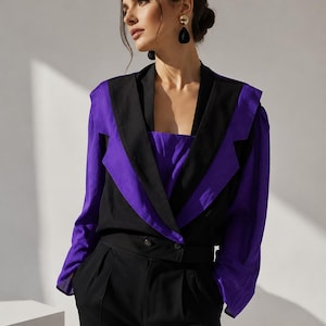 May include: A woman's outfit featuring a black and purple blazer with matching black pants. The blazer has a striking design with a purple front and black lapels. The pants are high-waisted with a button closure.