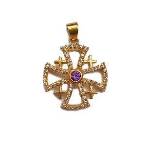 May include: A gold-toned pendant in the shape of a cross with a purple gemstone in the center. The cross is decorated with small clear stones.