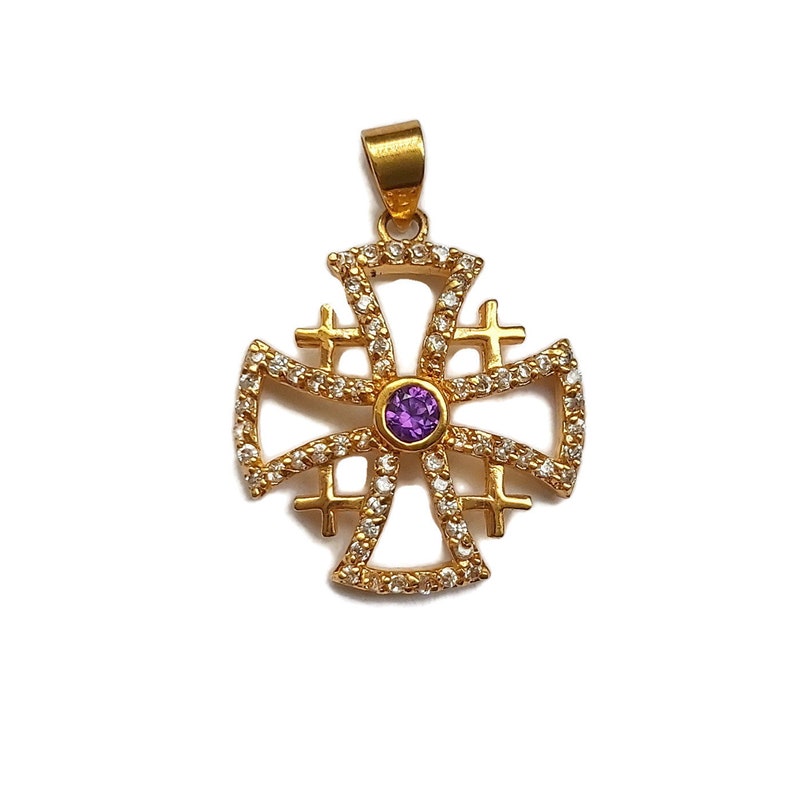 May include: A gold-toned pendant in the shape of a cross with a purple gemstone in the center. The cross is decorated with small clear stones.
