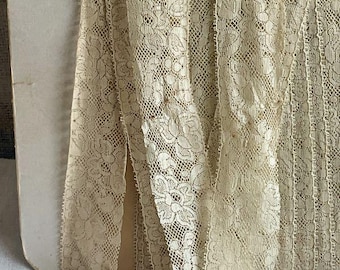 May include: A close-up of a beige lace trim with a delicate floral pattern. The lace is folded and arranged on a light brown surface.