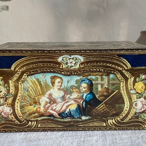 Puede incluir: Una caja rectangular de madera con un diseño pintado en oro y azul. La tapa presenta una escena pintada de dos figuras en un entorno de jardín. La caja está decorada con motivos florales y detalles intrincados.