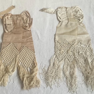 May include: Two vintage ivory sashes with bow details and fringed bottoms. The sashes are made of a silky material and feature intricate crochet lace. The bows are pleated, adding a touch of elegance to the design.