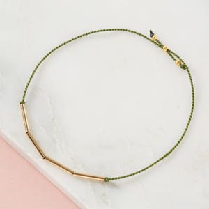 May include: A green string bracelet with gold tube beads.