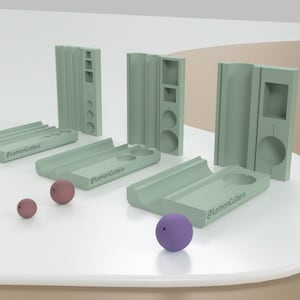 Puede incluir: Un conjunto de cuatro moldes de plástico verde para hacer esferas de diferentes tamaños. Los moldes están dispuestos en una fila sobre una superficie blanca. También hay cinco pequeñas esferas de diferentes colores en la superficie.