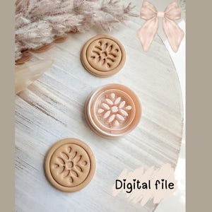 May include: Three beige, circular cookie cutters with floral designs are arranged on a white wooden surface. One cutter is open, revealing the floral imprint. The words "Digital file" are written in a script font.