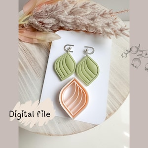 Puede incluir: Un par de pendientes en forma de hoja verde claro y un cortador de arcilla melocotón a juego se encuentran sobre una tarjeta blanca. Los pendientes tienen un diseño texturizado y acanalado. Las palabras "Digital file" están escritas en negro.