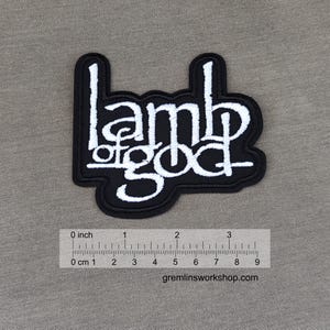 May include: Black and white embroidered patch with the words "Lamb of God" in a stylized font. The patch is approximately 2 inches wide.