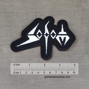 May include: Black and white embroidered patch with the word "SODOM" in a stylized font. The patch is approximately 4 inches wide and features a black border. The website gremlinsworkshop.com is visible at the bottom.